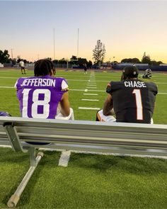 two football players sitting on a bench at the end of a field with their backs to each other