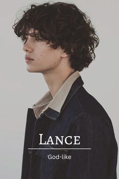 a young man with curly hair wearing a denim jacket and looking off to the side