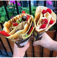 two people holding up some tacos with strawberries and raspberries on them