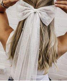 a woman wearing a white veil with pearls on it's head and holding her hair in the air