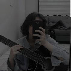 a person holding a guitar and taking a selfie with a cell phone in front of them