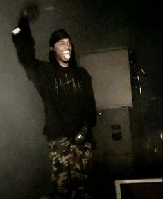 a man in camo pants and a black hoodie is holding his arms up