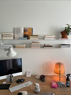 a wooden desk topped with a computer monitor next to a lamp and bookshelf