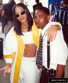 a man standing next to a woman wearing sunglasses and a yellow jacket with his arms around her