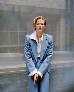 a woman in a blue suit and white shirt is leaning against a wall with her hands on her hips