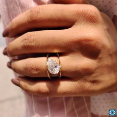 a woman's hand wearing a gold ring with a white diamond in the center