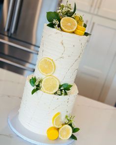 a three tiered white cake with lemons and greenery on the top layer