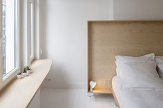 a bed sitting under a window next to a wooden shelf with two cups on it