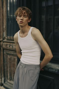 a young man standing in front of a window with his hands on his hips and looking at the camera