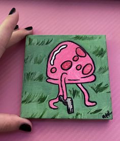 a painting of a pink mushroom on a green background is being held by a woman's hand