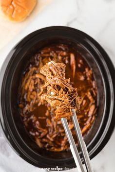 shredded meat in a slow cooker being held by two tongs over the bowl