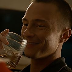 a man drinking from a glass with his hand on top of the glass and smiling