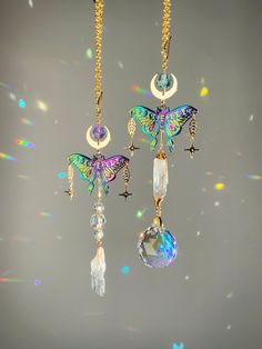 two necklaces hanging from chains with colorful butterflies on them and crystal balls in the background