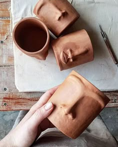 someone is holding their hand over some clay cups and spoons on a table with other items