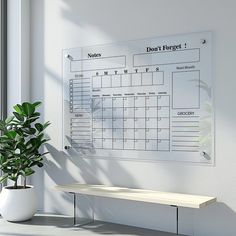 a desk with a potted plant next to a dry erase calendar on the wall