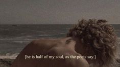 a woman sitting on top of a beach next to the ocean with her hair blowing in the wind