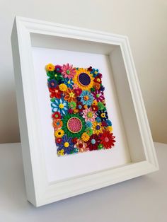 a white frame with colorful flowers in it on top of a table next to a wall