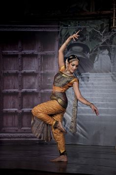 a woman is dancing on stage with her hands in the air while wearing an orange and gold outfit