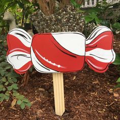 a red and white candy corn on a stick in front of some bushes with green leaves