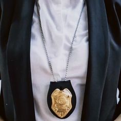 a woman wearing a black and gold necklace with a police badge on it's chest