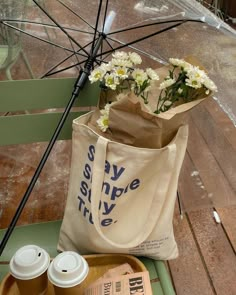 a bag with flowers in it sitting on a bench next to a cup of coffee and an umbrella