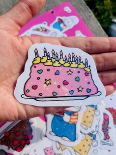 a hand holding a pink birthday cake sticker