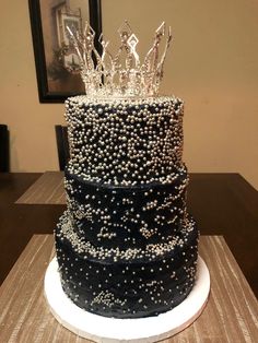 a three tiered black and white cake with silver decorations on the top, sitting on a table