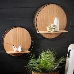 two round wooden shelves with plants and vases on them against a black wall, next to a potted plant