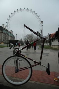 a bicycle parked on the side of a road next to a ferris wheel with people walking by