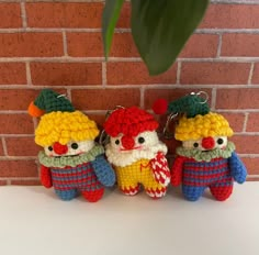 three small crocheted clowns are hanging on a brick wall next to a potted plant