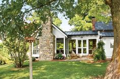 a white house with a black roof and windows on the front porch is surrounded by trees