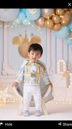 a little boy standing in front of a backdrop with gold and blue balloons on it