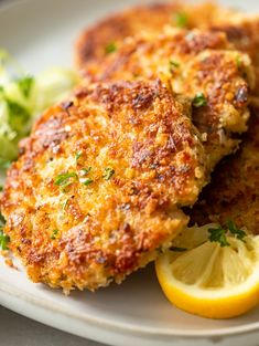 two crab cakes on a plate with lemon wedges