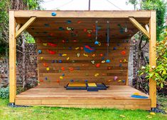 a wooden structure with climbing ropes on the side and a bench under it in front of a brick wall