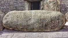 a large rock sitting in front of a stone building with carvings on it's side