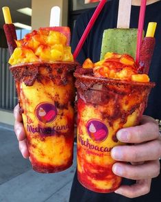 the man is holding two frozen drinks in their hands, both with different toppings