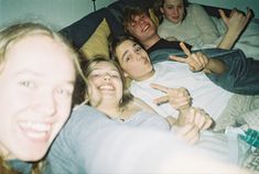 a group of people laying on top of a bed with one pointing at the camera