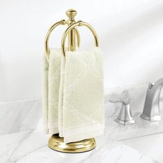 a gold towel holder with two white towels hanging from it's sides on a marble countertop