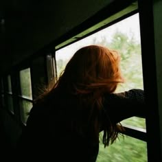 a woman looking out the window of a train car at green grass and trees in the distance