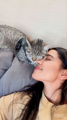 a woman laying on top of a bed next to a gray and white cat sleeping