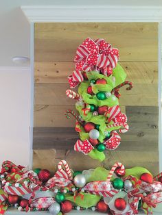 a christmas wreath on top of a mantel decorated with red, green and white ornaments