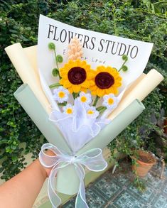 a bouquet of sunflowers is held up by someone's hand with a sign in the background