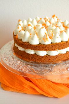 a carrot cake with white frosting and orange napkins on a glass platter