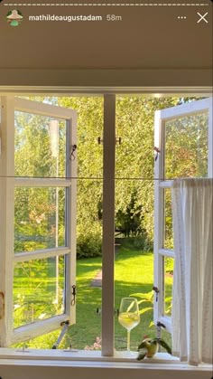 an open window with white curtains on the outside and green grass in the back ground