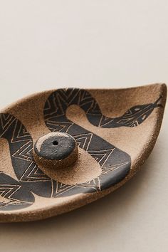 a black and brown ceramic dish with two buttons in it's center, sitting on a white surface