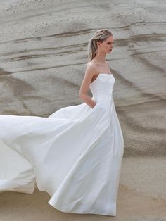 a woman in a white dress is walking on the sand with her long flowing skirt