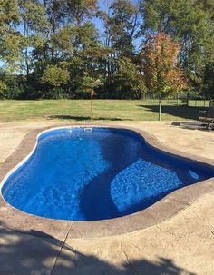 an empty swimming pool in the middle of a yard with chairs and trees around it