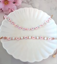 two pink and white beaded bracelets sitting on top of a plate next to flowers