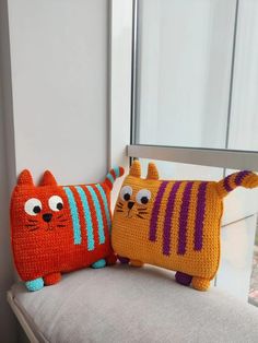 two crocheted cats sitting on top of a white couch next to each other