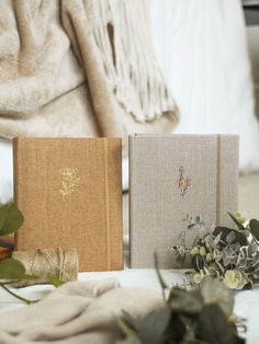 two notebooks sitting next to each other on a table with flowers and greenery